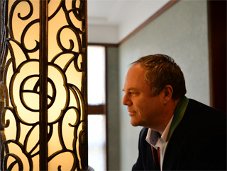 2階ホールの柱型の大きな照明を前に、特徴のあるパターンに見入るダイサム氏